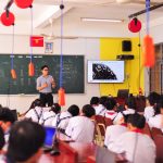 Professor conduz atividade interativa enquanto estudantes acompanham a aula em uma sala de aula.