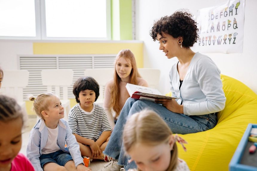 Professora lê um livro para crianças da pré-escola em uma sala de aula colorida.